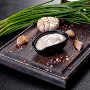 Garlic sauce in a ceramic black sauce with greenery on a wooden cutting board