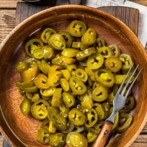 Jalapenos pickled and sliced, in old wooden plate . Wooden background. Top view